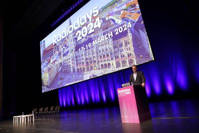 Peter Neigle on stage behind a lecturn at Radiodays 2023 announcing Munich as the venue for the event in 2024. A big screen behind him shows a photo of the city.