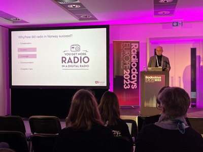 Ole Jørgen Torvmark stands at a lectern on stage at Radiodays Europe. To the left of him is a screen showing a slide headed "Why/how did radio in Norway succeed?" and a logo with a radio and the slogan "You get more RADIO in a digital radio"
