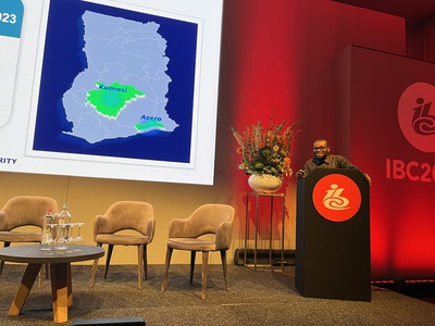 Edmund Fianko of the National Communications Agency in Ghana on stage at IBC in Amsterdam, in front of a screen showing a map of Ghana with the coverage area of DAB around Kumasi and Accra highlighted in green