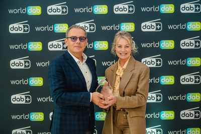 Mate Botica and Jacqueline Bierhorst Mate Botica (left) and Jacqueline Bierhorst holding the WorldDAB Award glass trophy in front of a panel with WorldDAB logos