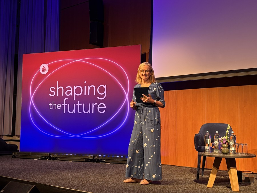 WorldDAB Project Director Bernie ONeill on stage at IBC2025 holding an iPad in front of the IBC logo with the words "shaping the future"
